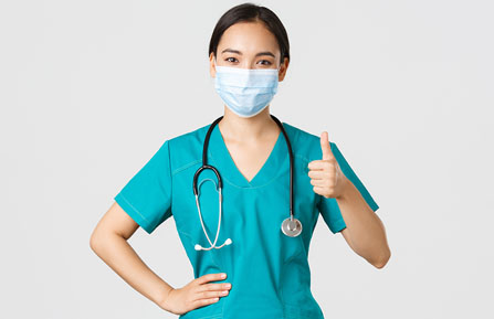 health professional in scrubs and mask with her thumb up