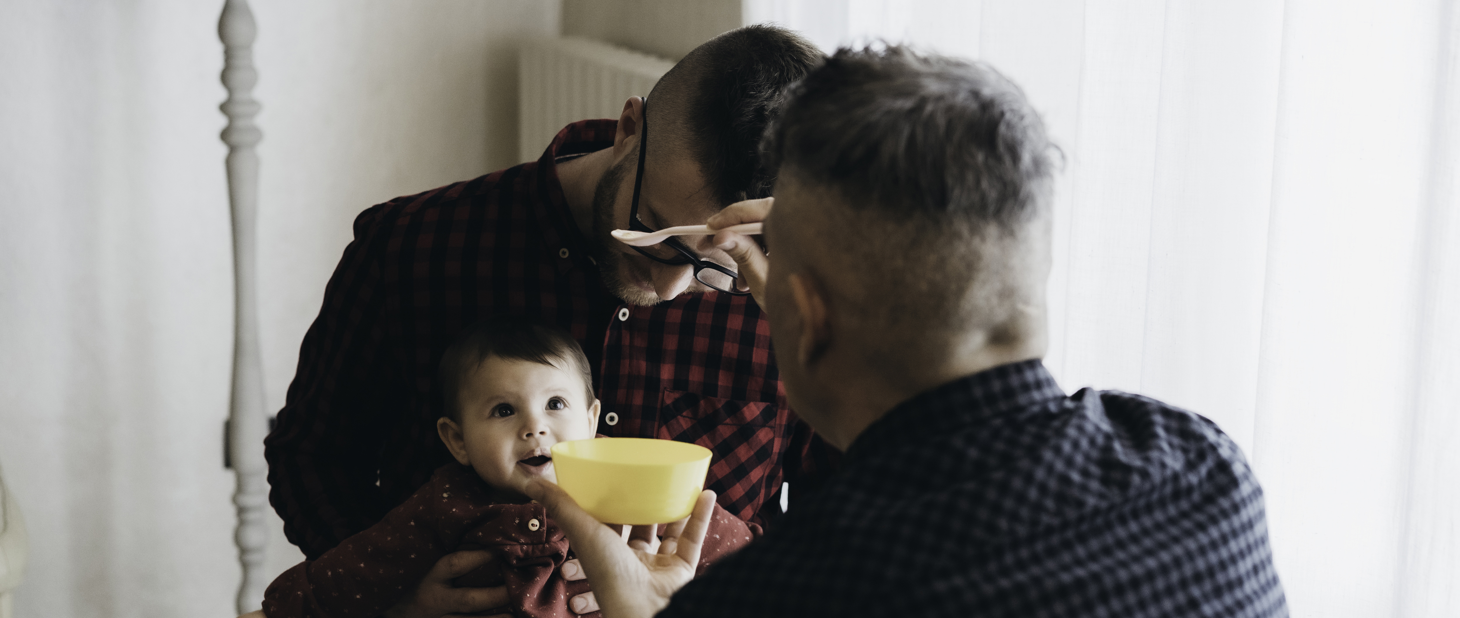 A male same-sex couple feeding their infant.